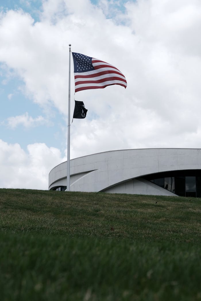 American flag waves proudly beside a modern architectural building under a vibrant blue sky.